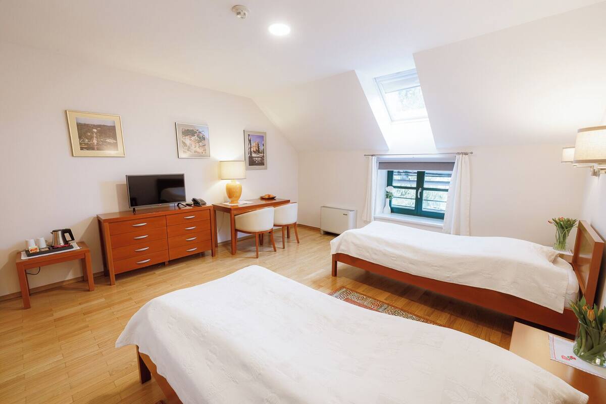 Une chambre d’hôtel avec deux lits, un bureau avec une chaise, une télévision, une lampe et une fenêtre donnant sur un paysage agréable.