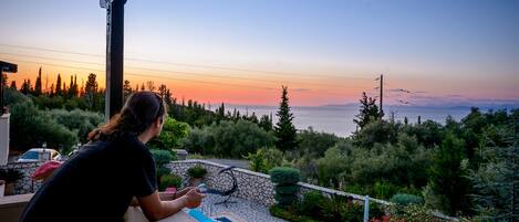 A balcony with a view of the sunset over a mountainous landscape.