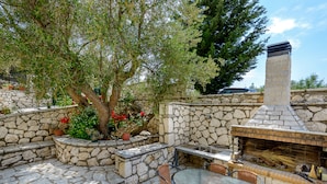 An outdoor patio with stone flooring, a glass table, wicker chairs, and a brick fireplace.