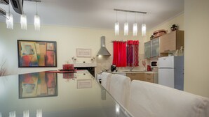 A modern kitchen with a glass dining table, pendant lights, and a red curtain.