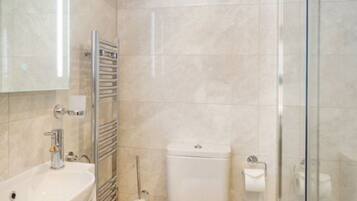 Un baño moderno con cabina de ducha de vidrio, un lavabo blanco y un inodoro.