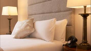 A hotel room with a large bed, two bedside lamps, and a telephone on a wooden nightstand.