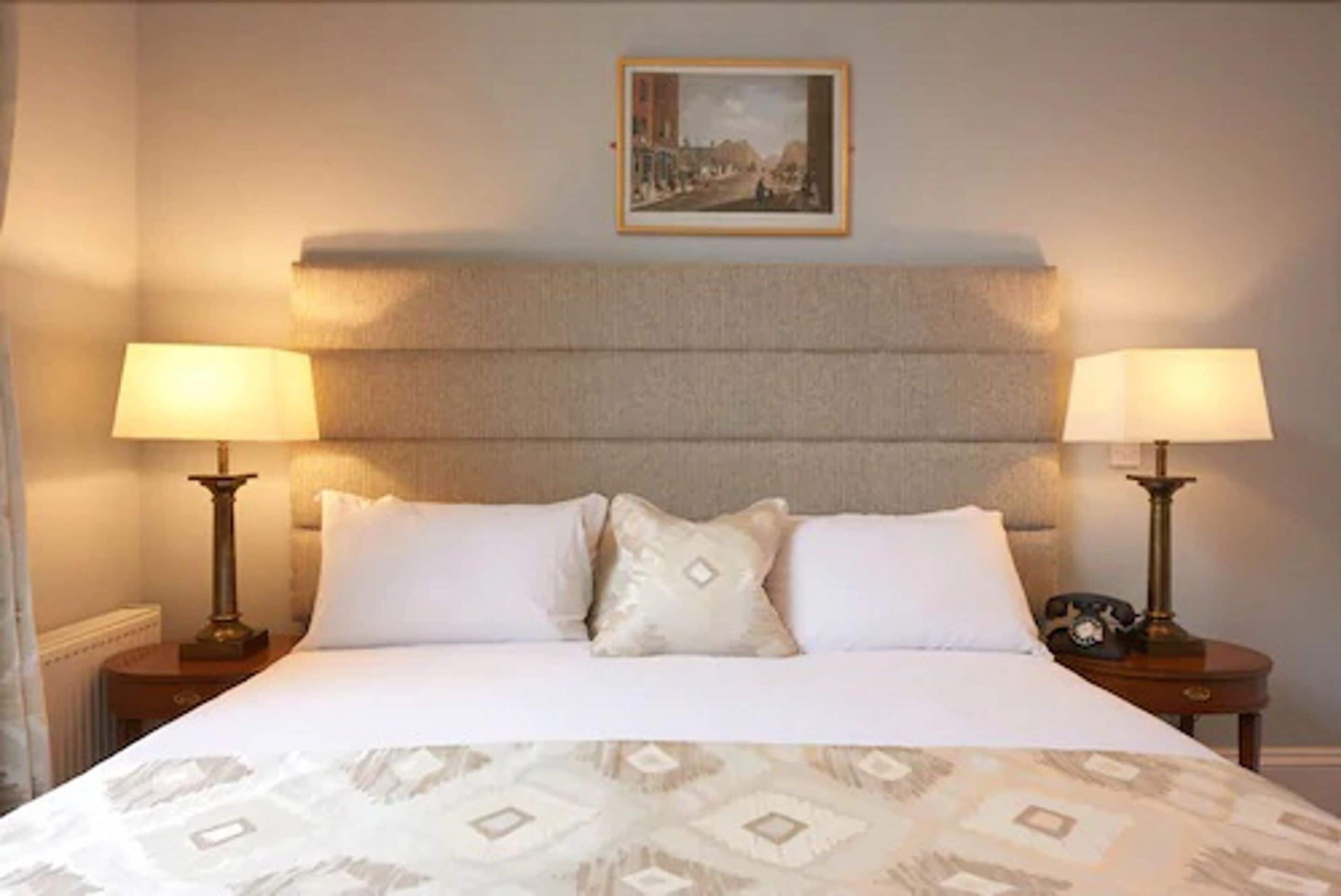 A neatly made bed with a patterned bedspread, two bedside lamps, a framed picture on the wall, and a small table with a telephone.