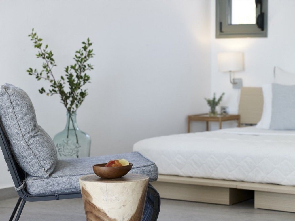 Ein Schlafzimmer mit einem Bett, einem Nachttisch, einem Sessel und einem kleinen Holzschemel.