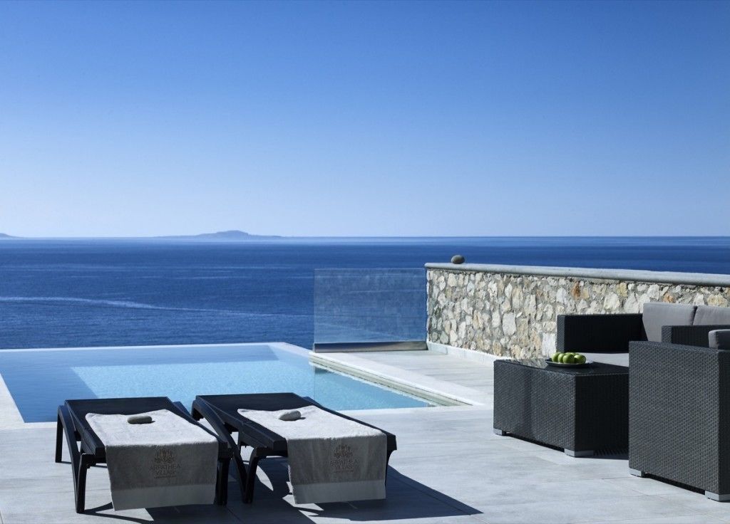 An infinity pool with lounge chairs and a stone wall, overlooking the sea.