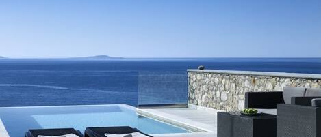 An infinity pool with lounge chairs and a stone wall, overlooking the sea.