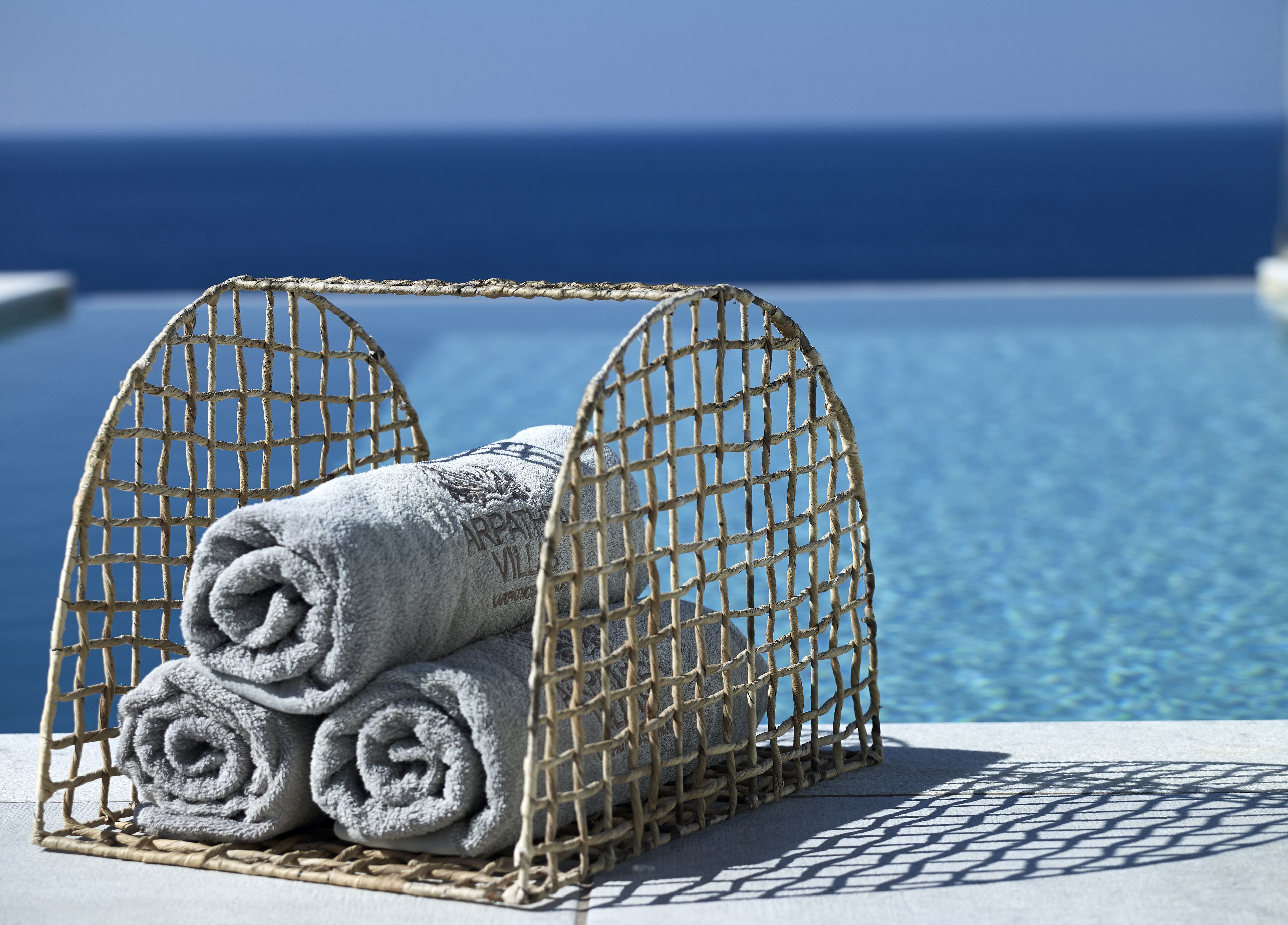 A wicker basket with rolled towels placed on a poolside area.
