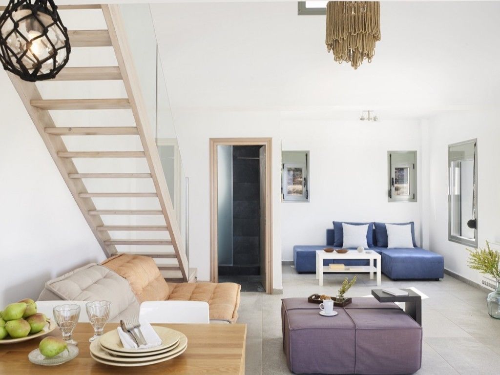 A modern living room with a wooden staircase, a blue sofa set, and a dining area with a wooden table and plates.