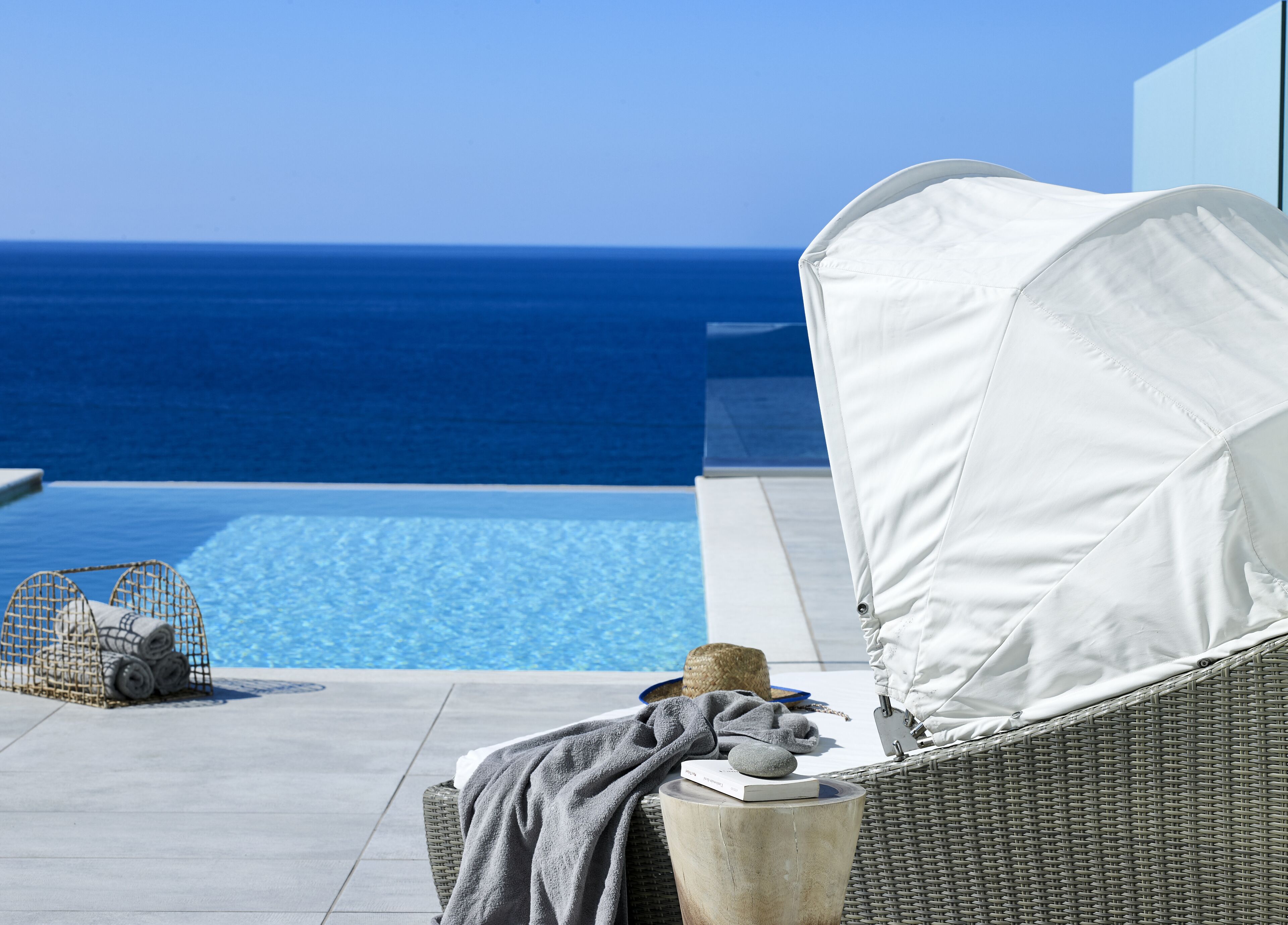 A wicker lounge chair with a white canopy overlooking a pool and the ocean.