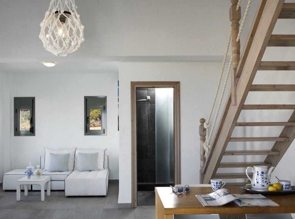 A modern living room with a white sofa, a wooden table with a newspaper, and a staircase with a rope railing.