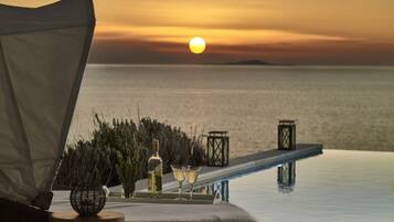 A sunset view from an infinity pool with a lounge chair, a bottle of wine, and two glasses.