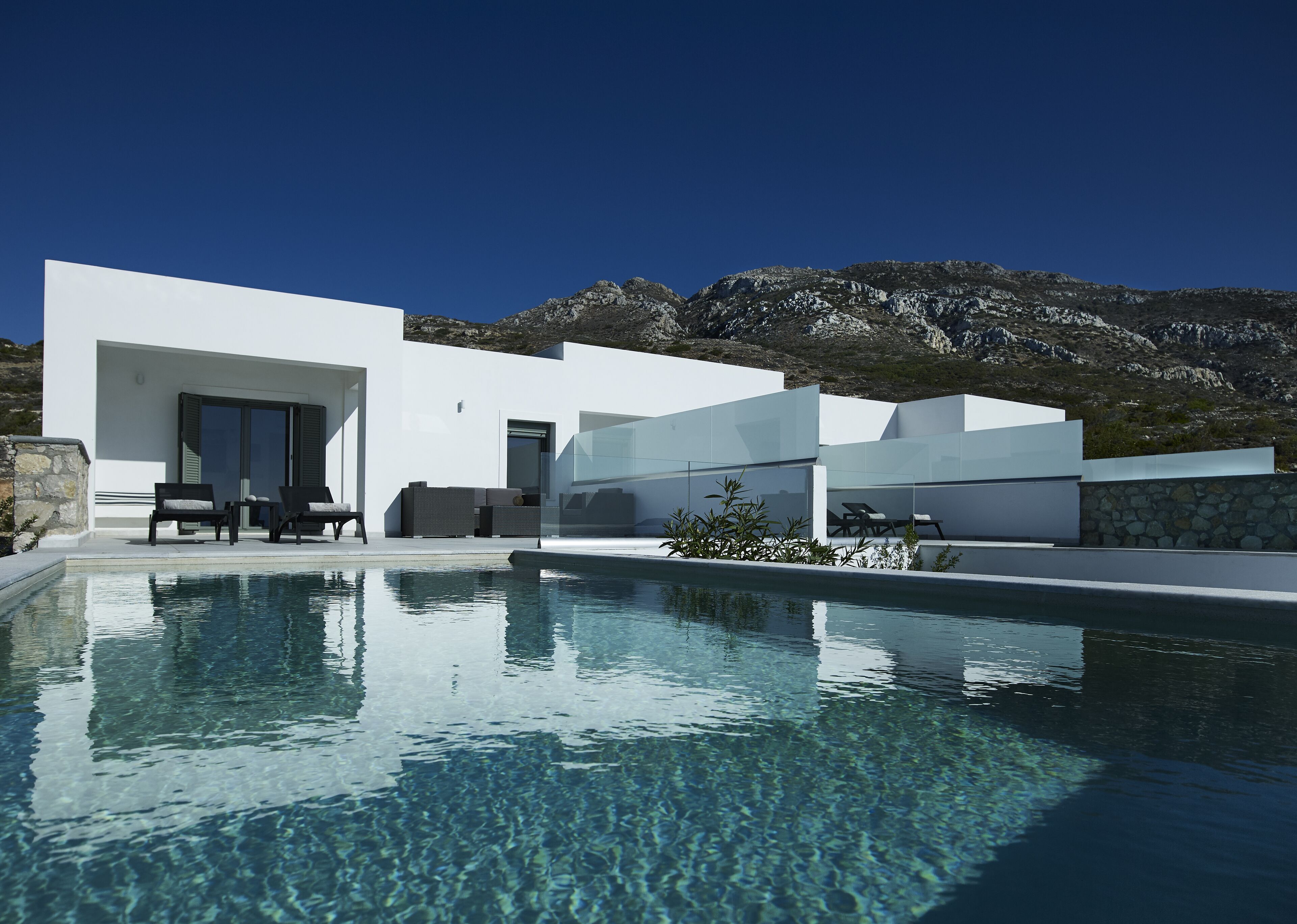 A modern poolside area with a clear pool, outdoor seating, and a mountainous backdrop.
