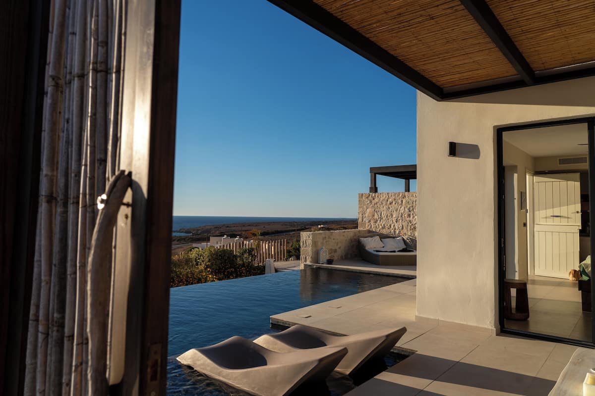 Ein Infinity-Pool mit Liegestühlen, einer Steinmauer und Blick auf den Ozean.