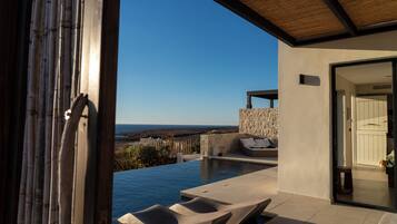 Una piscina infinita con sillones de descanso, un muro de piedra y vista al océano.