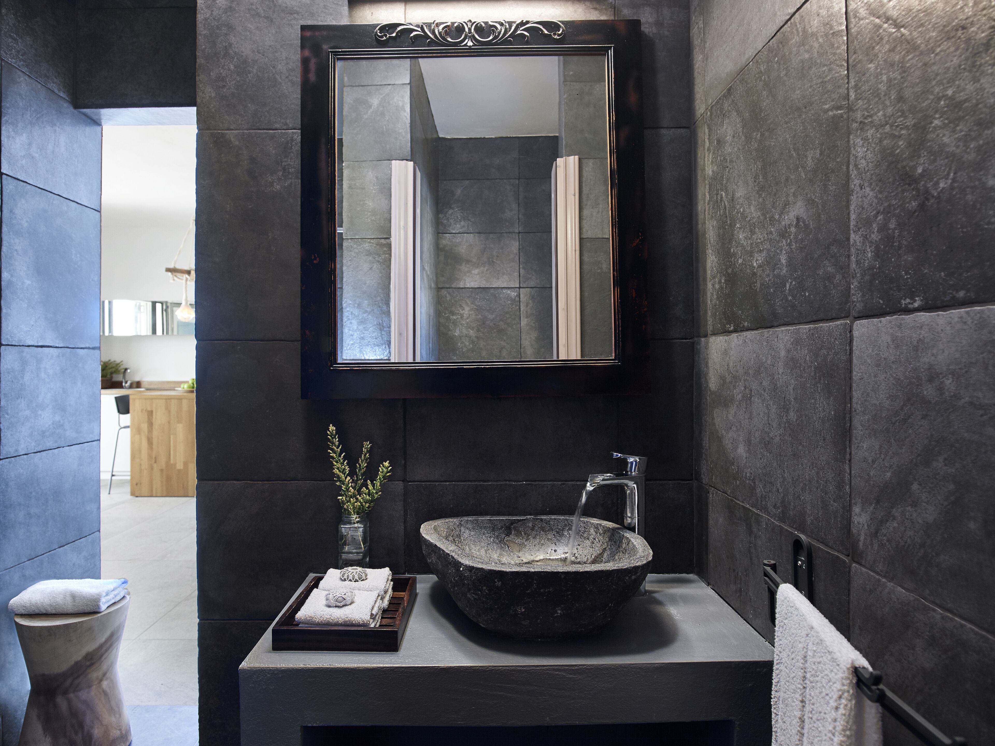 A modern bathroom with a stone sink, a mirror, and a small plant.