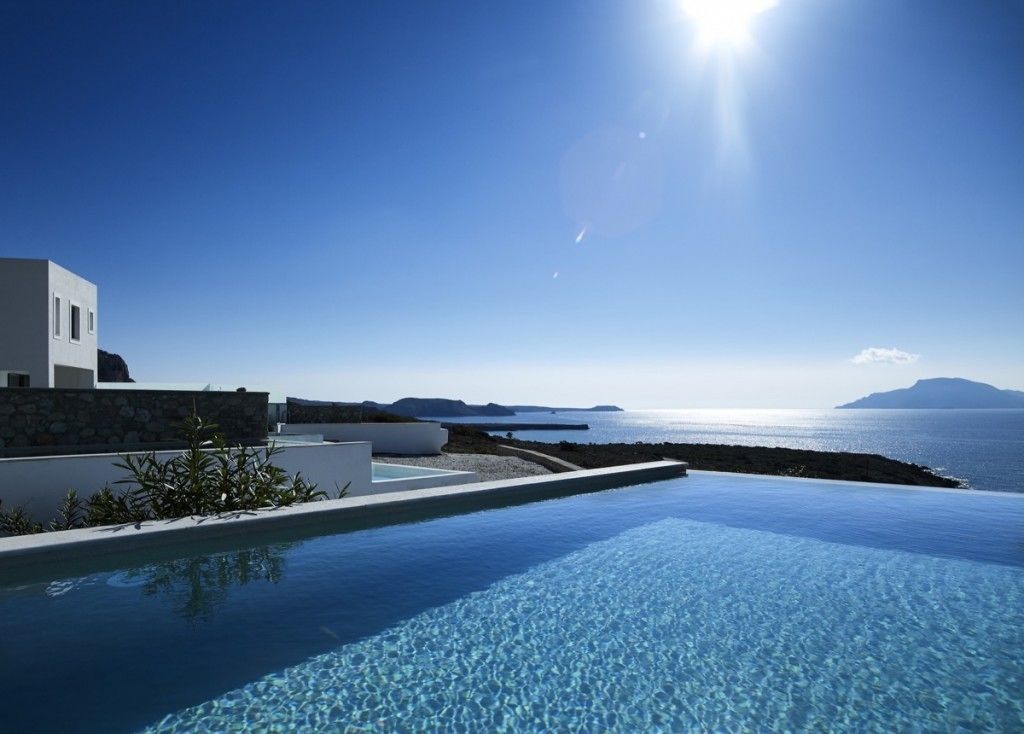 Una piscina infinita moderna con agua azul cristalina, un edificio blanco y vistas al mar y a islas distantes.