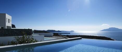 A modern infinity pool with clear blue water, a white building, and a view of the sea and distant islands.