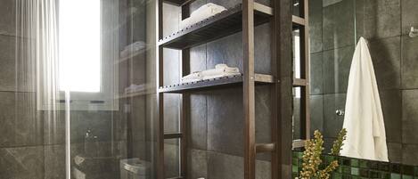 A modern bathroom with a glass shower enclosure, a wooden vanity with a bowl sink, and a shelf unit with towels.