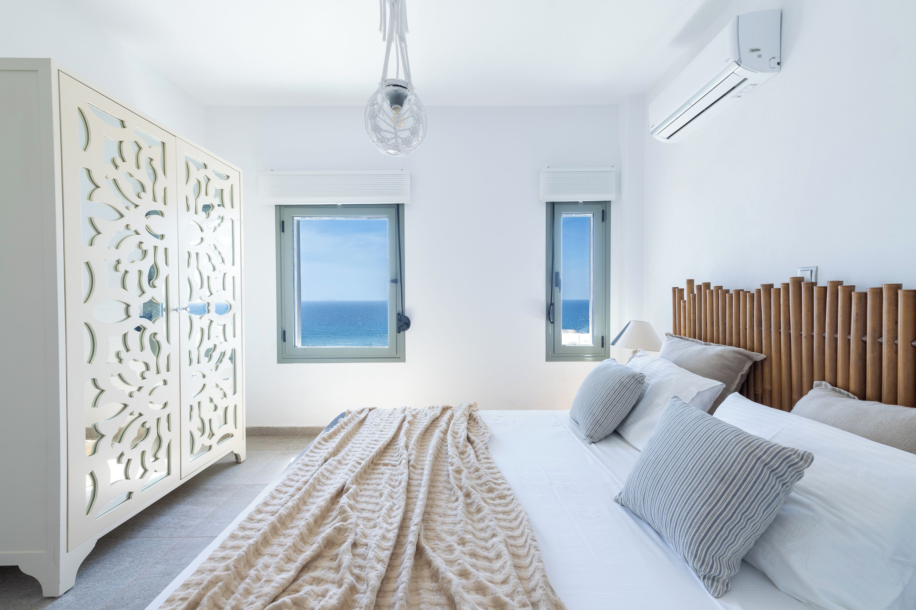 Une chambre moderne avec un grand lit, deux fenêtres donnant sur l’océan, un élément de séparation décoratif blanc et un luminaire au plafond.