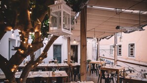 Un'area pranzo all'aperto con tavoli e sedie in legno, luci a stringa e lanterne appese.