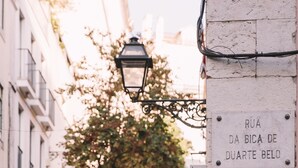 Una stretta via con un lampione, una cassetta delle lettere e un cartello che riporta la scritta "Rua da Bica de Duarte Belo".