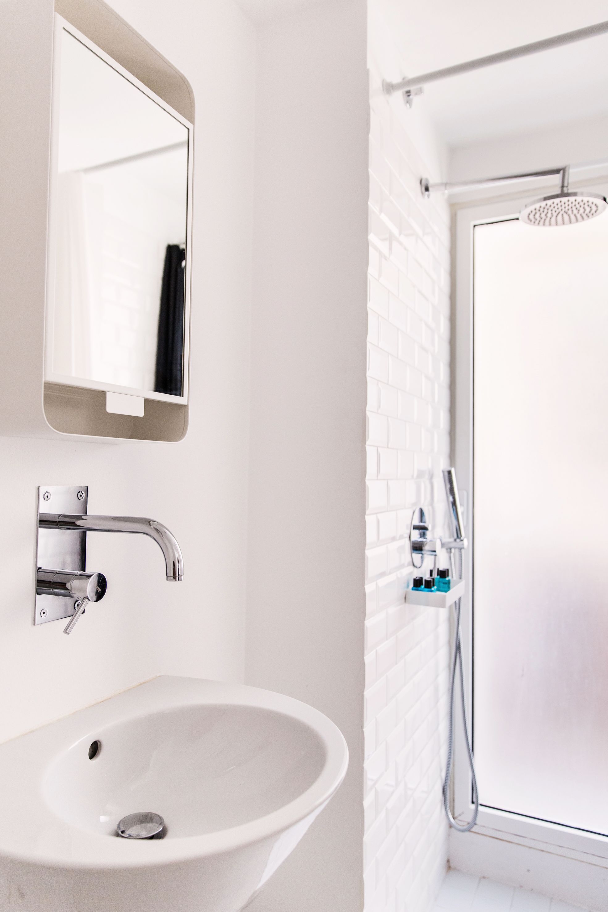 A bathroom with a white sink, a mirror, a shower with a glass door, and a white tiled wall.