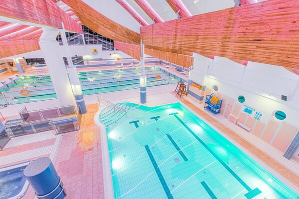 A multi-level indoor swimming pool with various lanes and a seating area.