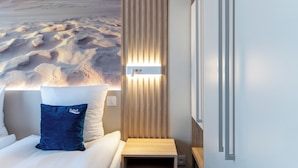 Een slaapkamer met een bed, kussens, een nachtkastje, een wandlamp en uitzicht op een strand.