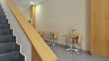 A staircase with a wooden handrail leading to a dining area with tables and chairs.