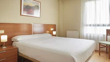 Habitación de hotel con una cama grande, lámparas de noche, una mesita de madera, una silla y un cuadro en la pared.