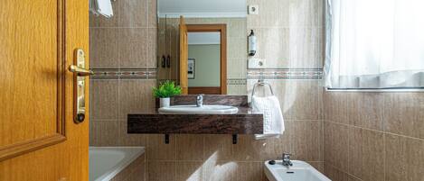 Un baño moderno con puerta de madera, un lavamanos con espejo encima, un bidé y una planta en maceta sobre la encimera.