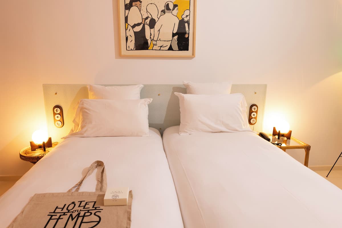 A double bed with white linens and two bedside tables with lamps.