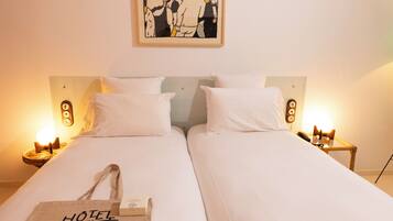 A double bed with white linens and two bedside tables with lamps.