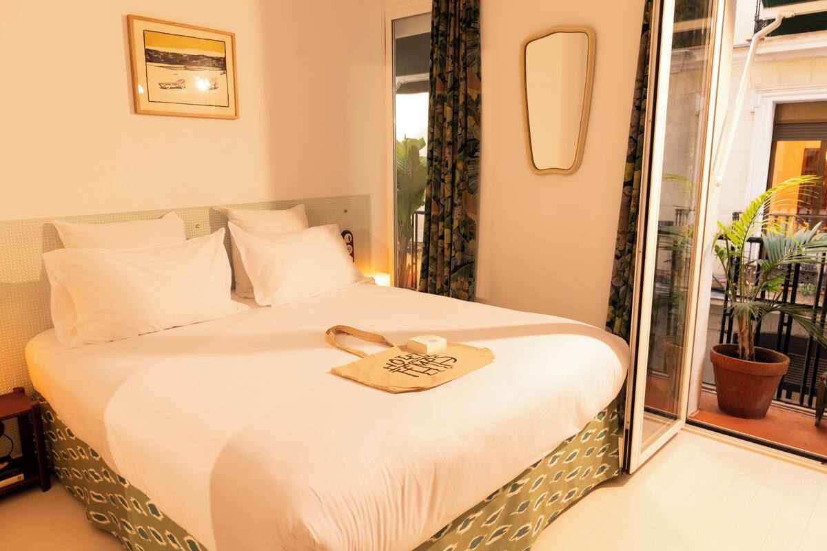 A hotel room with a large bed, a nightstand, a mirror, and a view of the outside balcony.