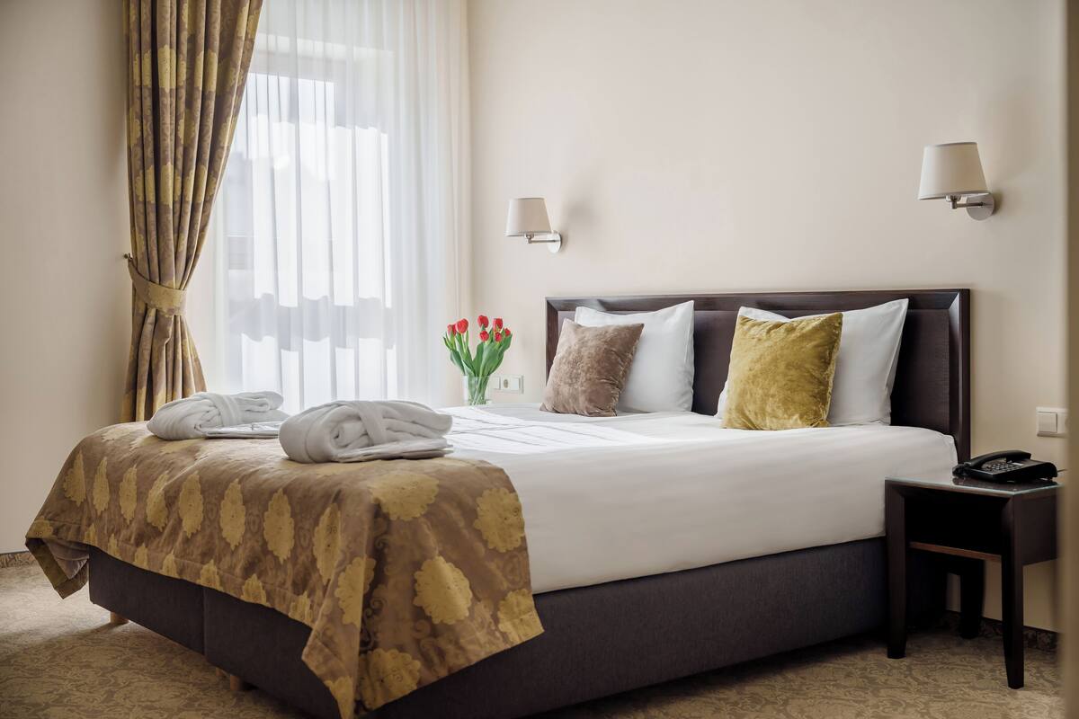 A neatly made bed with a patterned bedspread, a bedside lamp, and a telephone on a nightstand.