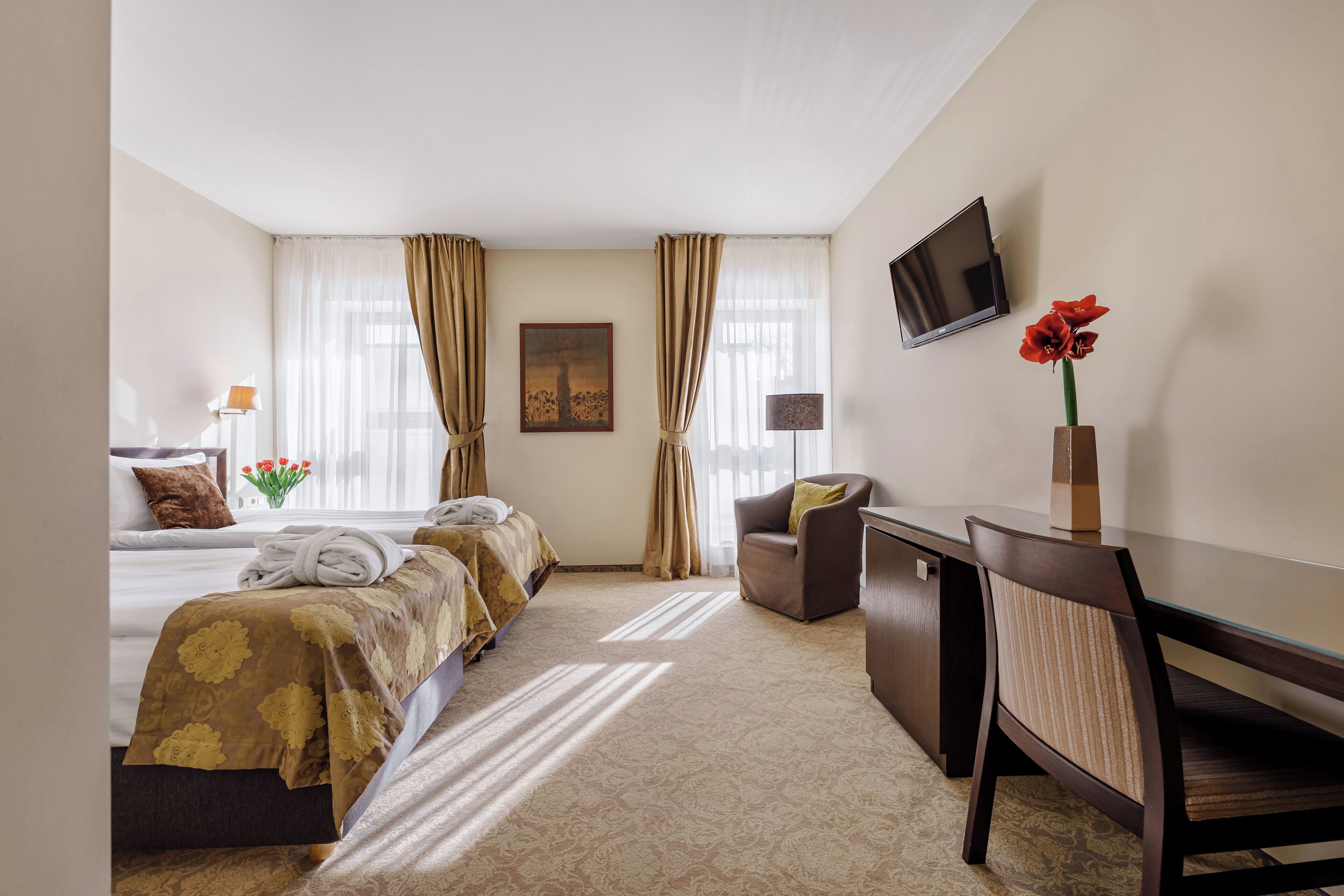 Een hotelkamer met twee bedden, een bureau, een stoel, een televisie en een schilderij aan de muur.