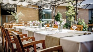 Restaurante com mesas ao ar livre, toalhas brancas e cadeiras de madeira.