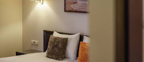 A hotel room with a bed, a nightstand, a wall-mounted lamp, and a framed picture on the wall.