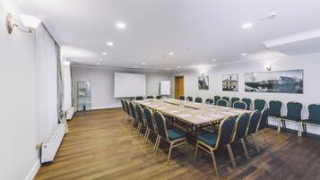 Een vergaderzaal met een lange tafel, stoelen, een whiteboard en kunstwerken aan de muur.