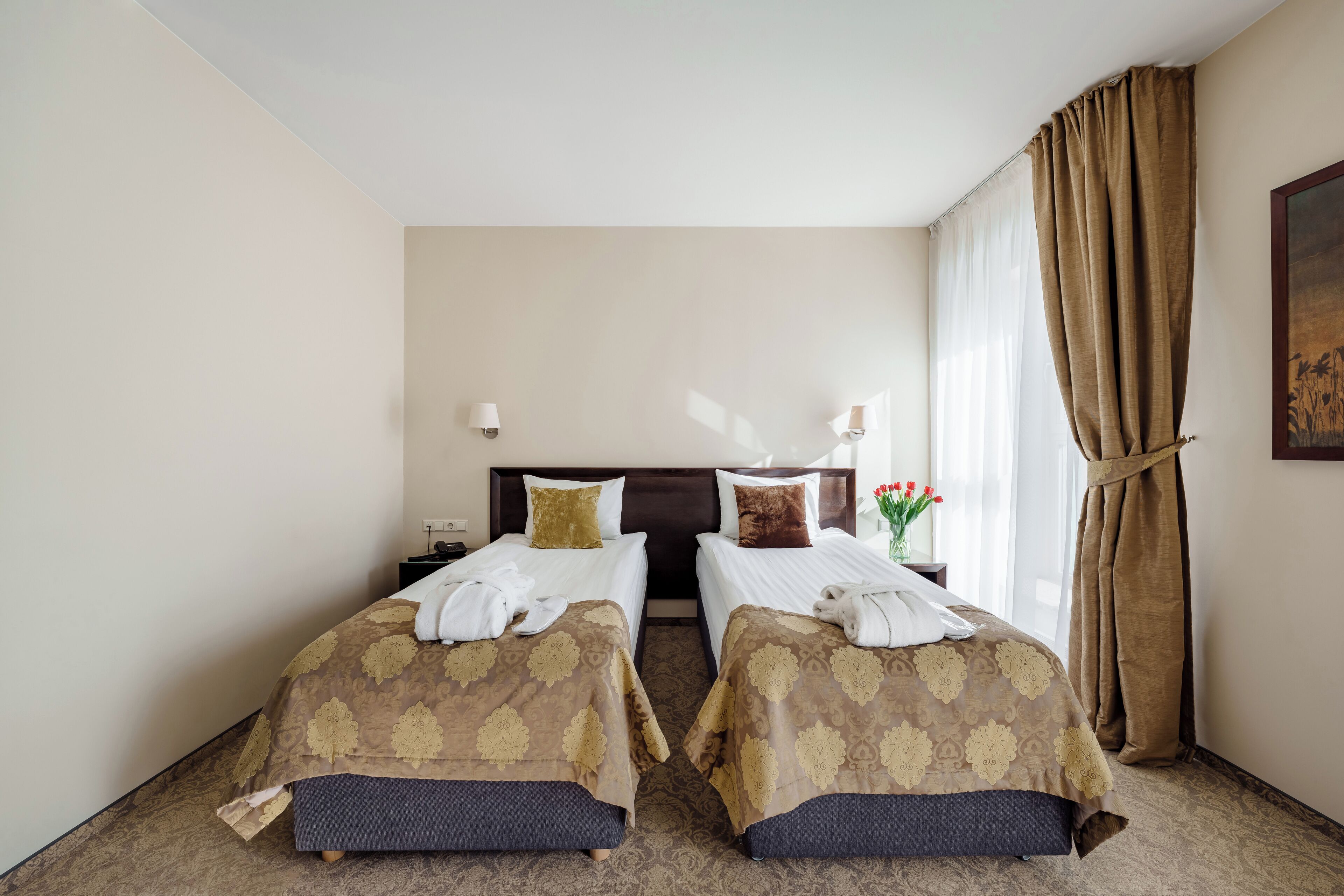 Habitación de hotel con dos camas, una mesita de noche, una lámpara y una ventana con cortinas.