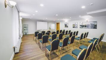 A conference room with rows of teal chairs, a whiteboard, and a projector screen.