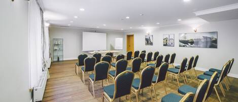 Une salle de conférence avec des rangées de chaises de couleur turquoise, un tableau blanc et un écran de projection.