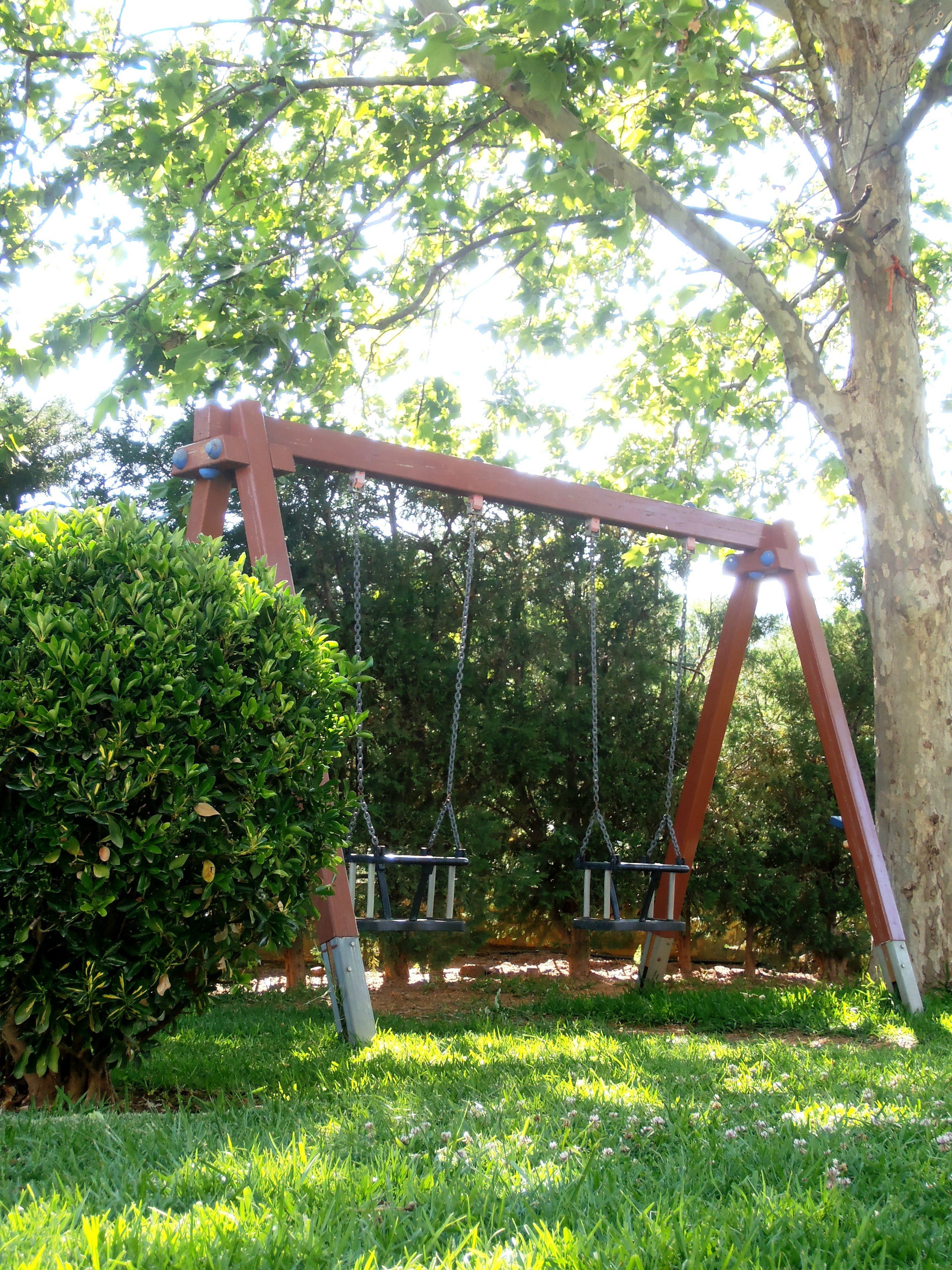 A swing set with two swings, surrounded by greenery and trees.