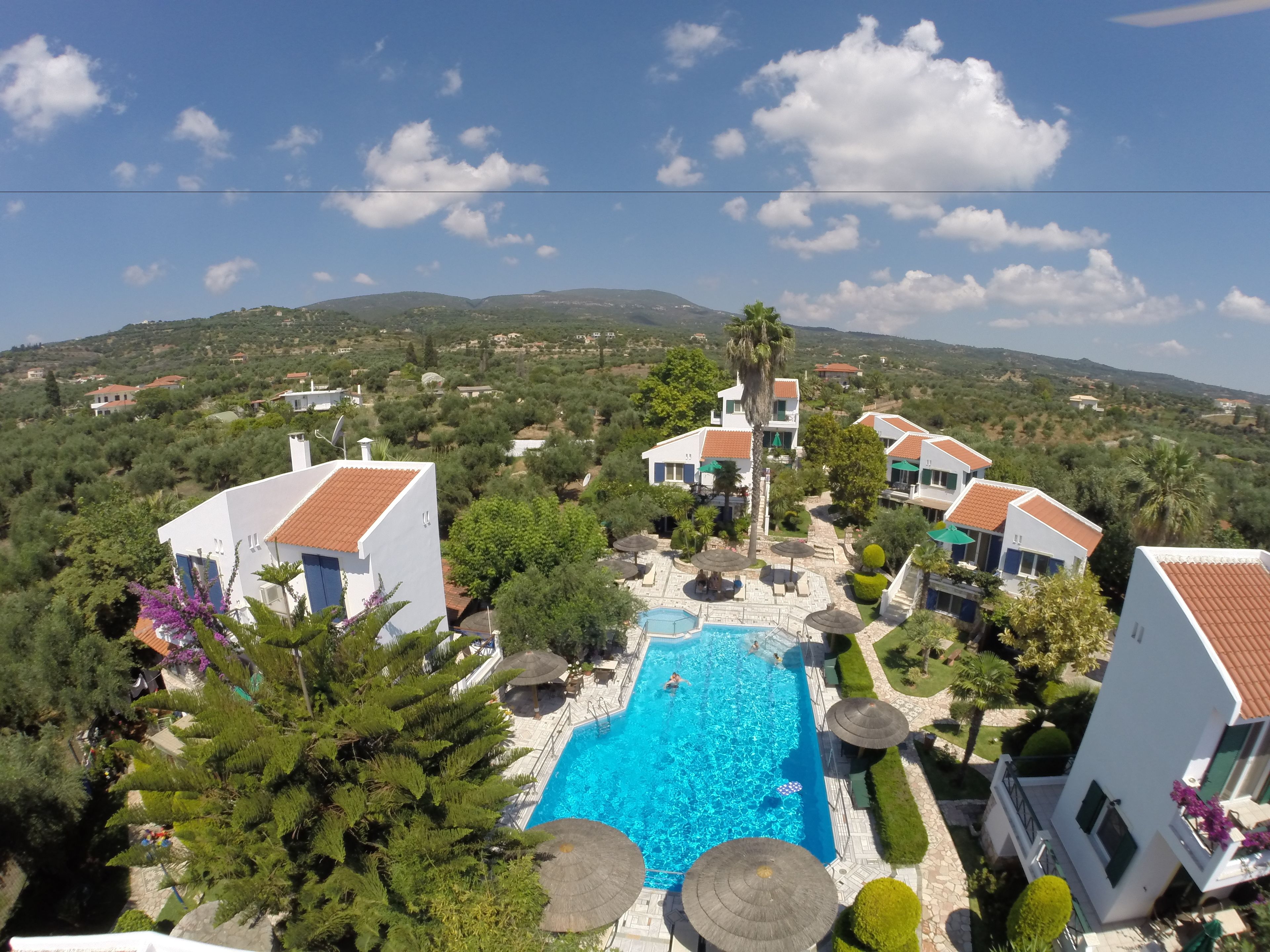 A resort with a swimming pool surrounded by lush greenery and white buildings with red-tiled roofs.