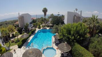 Una piscina rodeada de sillones de playa y sombrillas, con vista al mar y palmeras.