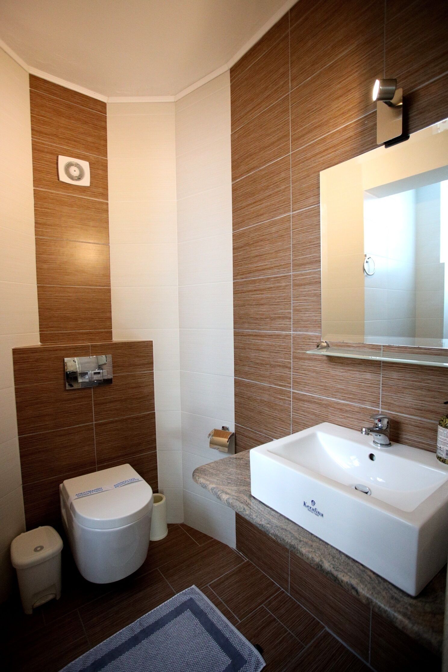 Een moderne badkamer met een witte wastafel, toilet en een spiegel boven de wastafel.