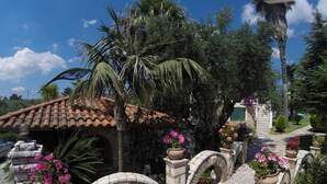 A courtyard with a stone archway, a tiled roof, and potted flowers. - Paris Village (Messini)