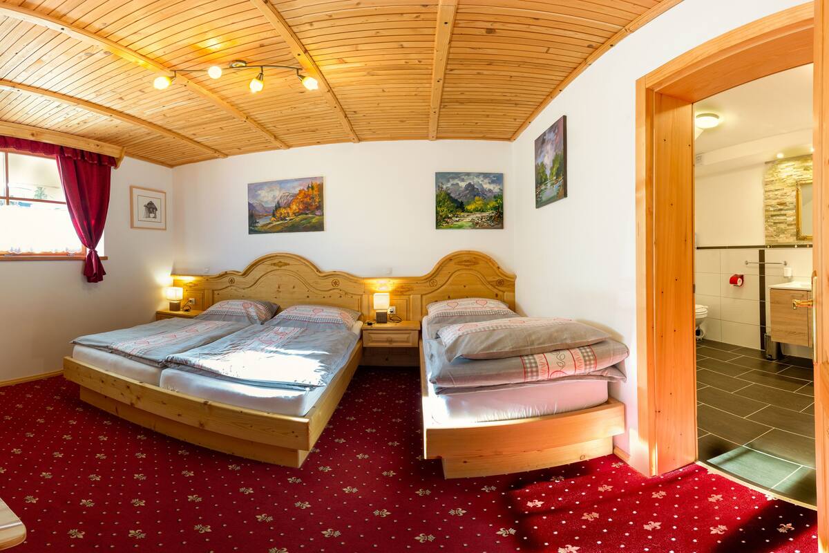 Un dormitorio acogedor con dos camas de madera, una alfombra roja y un techo de madera.