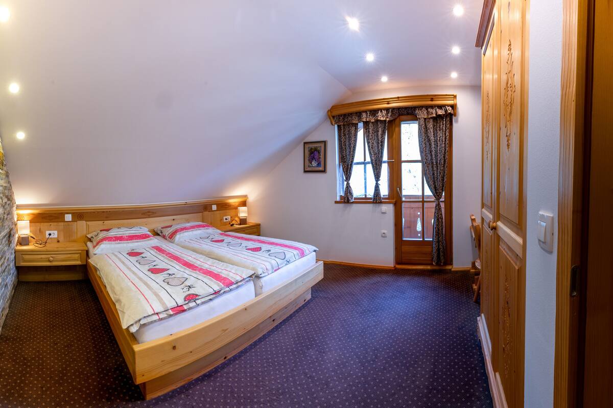 Un dormitorio con cama de madera, pared de piedra, armario de madera y ventana con cortinas.