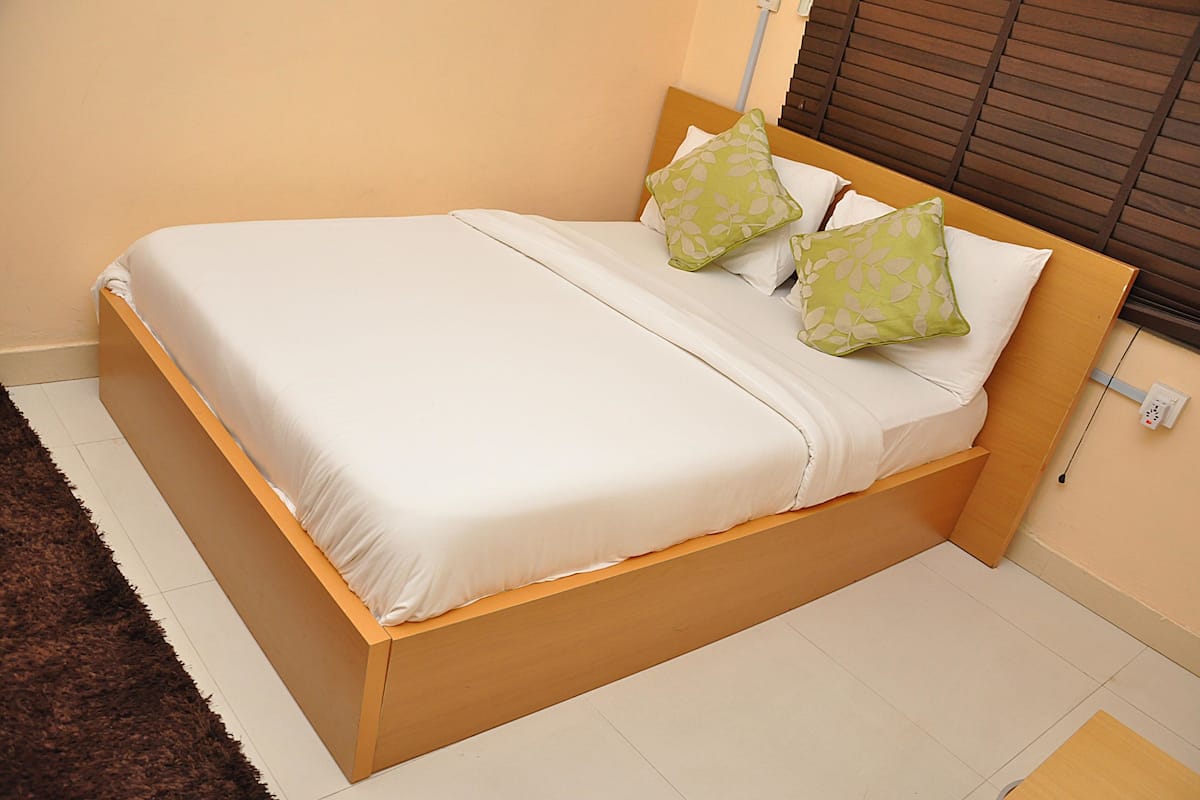 A bed with a wooden frame, white bedding, and two green patterned pillows.